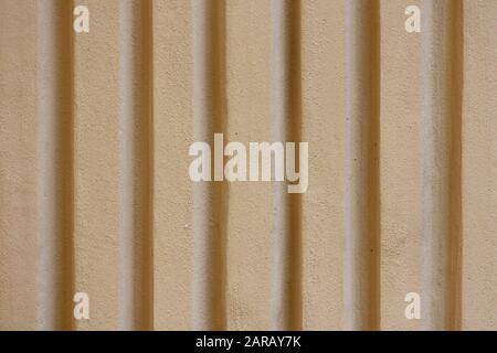 Wavy corrugated metal sheet with vertical bars painted with dark yellow paint on side of shipping container texture background wallpaper Stock Photo