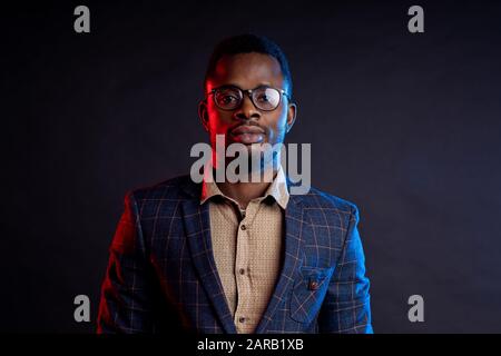 Closeup portrait of young handsome confident serious bearded african businessman in glasses, wearing shirt, checked suit, looking at camera, standing Stock Photo