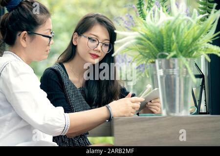 two asian woman with smart phone in hand talking  in home living room with happiness face Stock Photo