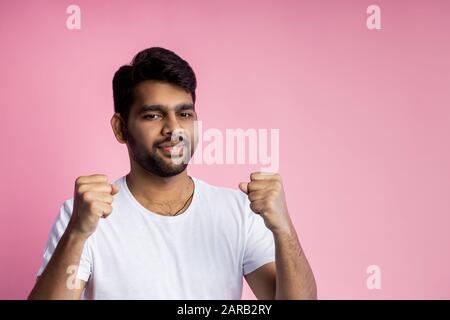 People, success, win, good news and celebration. Happy successful young indian male raising hands, clenching fists in triumph, celebrating victory, we Stock Photo