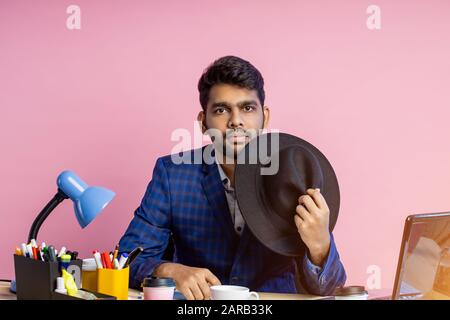 Indian businessman wearing suit, black hat, looking at screen of mobile phone, waiting for important call, reading news, sending email, sitting at wor Stock Photo