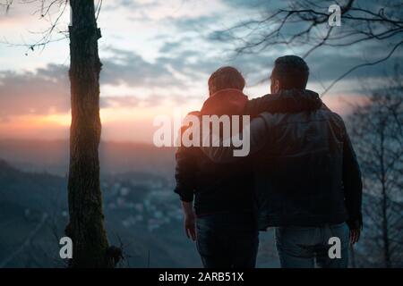 Rear view of friends watching the sunset over the cliff with city Stock Photo
