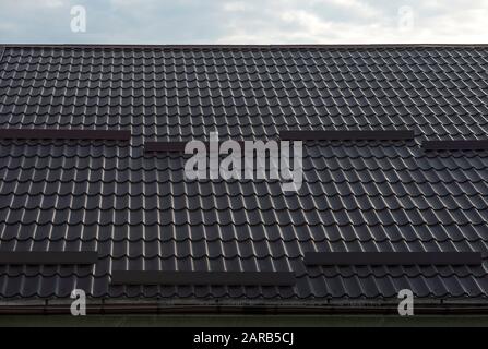 Roof slope covered by tile effect metal sheets of dark brown color. Stock Photo