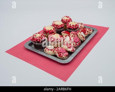 Rustic silver tray full of Valentine’s Day cupcakes and thumbprint cookies, on a pink placement with a white background.  The cupcakes and cookies are Stock Photo