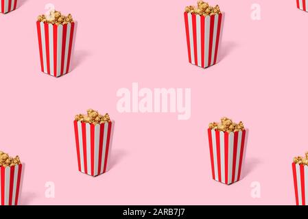 Movie Popcorn in striped red bucket isolated on pink background. Seamless pattern on a pink background. Stock Photo