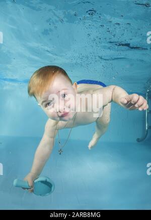 Funny baby boy with toy plays underwater with fun in the pool. Healthy family lifestyle and children water sports activity. Child development, disease