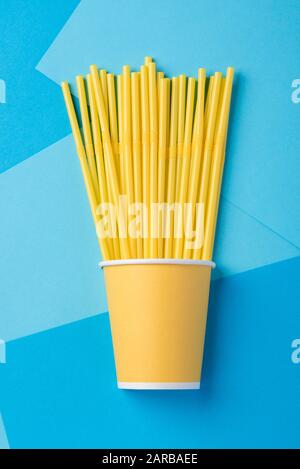 Yellow straws for a party in paper cups on a bright blue background Stock Photo