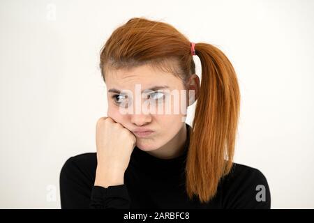 Closeup portrait of a sad redhead teenage girl with childish hairstyle looking offended isolated on white backround. Stock Photo