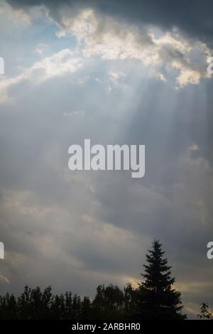 Bright rays of sun spreading from behind dark stormy clouds background. Stock Photo