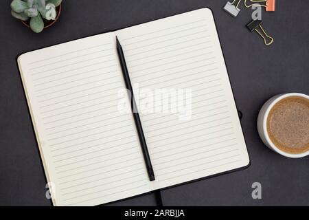 Open notebook with empty page and coffee cup. Table top, work space on dark background. Creative flat lay. Stock Photo