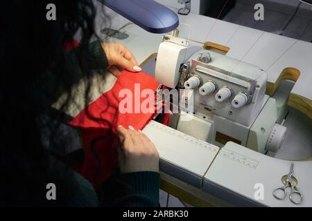 Young woman using professional overlock sewing machine in workshop. Equipment for edging, hemming or seaming clothes at tailors shop Stock Photo