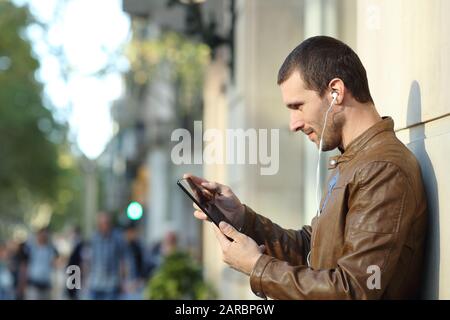 Side view portrait of an adult man wearing earphones using a tablet in the street Stock Photo