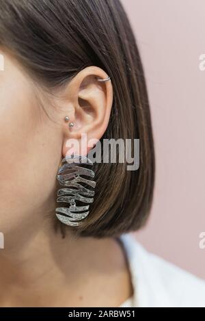 trendy stylish silver earrings on the girl's ear with bob haircut. Pastel pink background. Stock Photo
