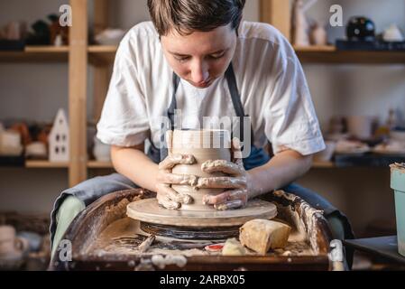 Potter working on a Potter's wheel making a vase. Young woman forming the clay with her hands creating jug in a workshop. Stock Photo