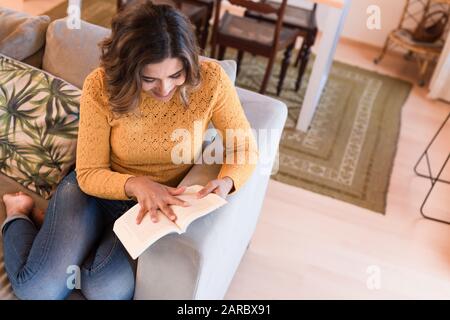 Woman At Home Lying On Reading Book on sofa Stock Photo