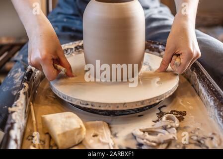 Woman potter working on a Potter's wheel making a vase. Master pulls the jug off the circle wetting it with water and gently holding it in hands Stock Photo