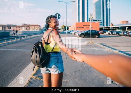 Young beautiful black woman outdoor holding hand walking on the road, smiling - follow me, travelling, discovering concept Stock Photo