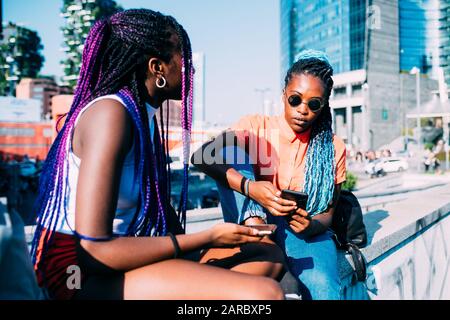 Two women sisters sitting outdoor talking and using smartphone - phubbing, isolation, technology concept Stock Photo