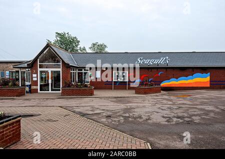 Flowers bloom in raised brick enclosed beds on an herringbone patterned forecourt outside the brightly painted Seagull's restaurant under a misty sky Stock Photo