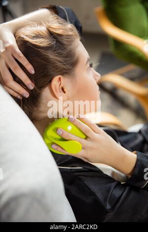 Beauty Day. Woman wearing silk robe doing her daily skincare routine at home. Sitting on sofa, massaging neck's skin with cosmetic's roller, smiling. Concept of beauty, self-care, cosmetics, youth. Stock Photo