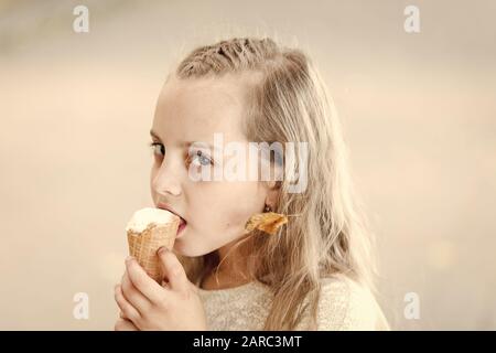 Lick frozen yoghurt. Girl sweet tooth eat ice cream. Kid with ice cream cone in hand. Child white ice cream in waffle cone. Summer treats concept. Happy childhood. Buy ice cream street food. Stock Photo