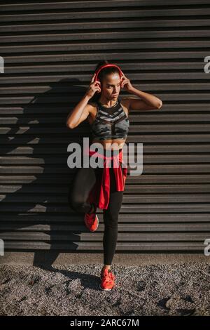 Young fit black girl in sports bra takes her jacket off on green