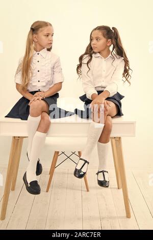 Why are you sad. Schoolgirls tidy hairstyle relaxing having rest. School uniform. School club. Little schoolgirls classmates friendly kids. Schoolgirls friends sit on desk. Best friends relaxing. Stock Photo