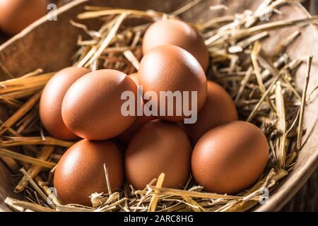 Fresh raw eggs in straw and wooden bowl on rustic wooden table Stock Photo