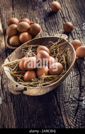 Fresh raw eggs in straw and wooden bowl on rustic wooden table Stock Photo