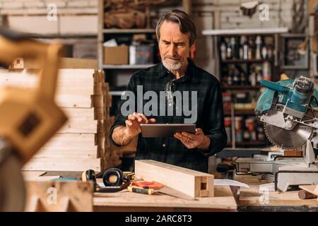 Senior carpenter using a digital tablet in his workshop Stock Photo