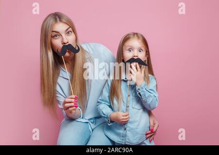 Mother and her daughter girl holding paper mustache on sticks. Stock Photo