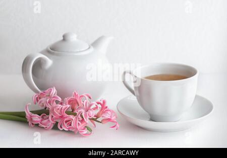White ceramic teapot and cup with tea. Hyacinth flower on a white background. Selective focus. Breakfast concept. Close up. Stock Photo