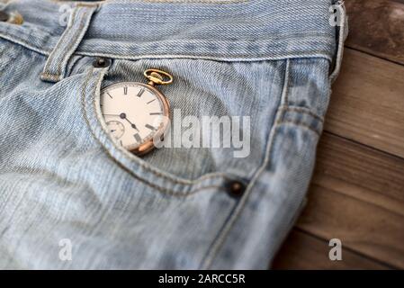 Clock in a jeans pocket on a wooden surface - time management concept Stock Photo