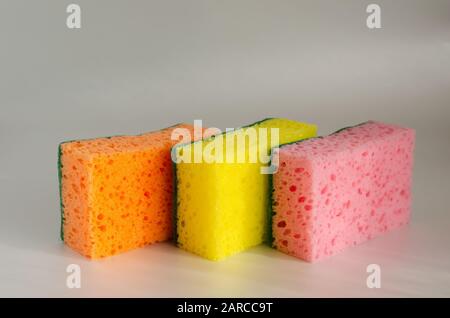 Kitchen sponges on a light background. Three multi-colored new sponges for washing dishes. Close-up. Selective focus. Landscape photo arrangement. Stock Photo