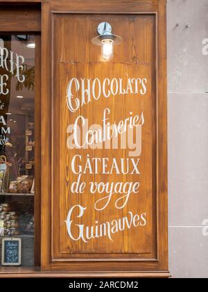 A wooden board or window shutter outside a french chocolate shop with writing advertising chocolates, confiseries, gateaux de voyage and other sweets Stock Photo