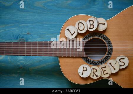 guitar on teal wooden background with wood pieces on it lettering the german word: LOBPREIS Stock Photo