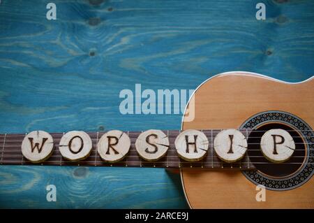 guitar on teal wooden background with wood pieces on it lettering the word: WORSHIP Stock Photo