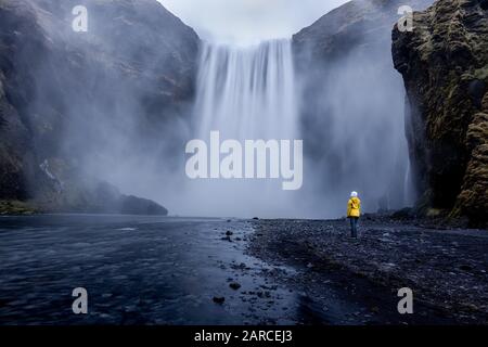 Person wearing a yellow jacket standing at the mesmerizing waterfall Stock Photo
