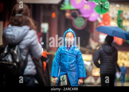 Shanghai, China, 25th Jan 2020, A woman wearing a masks walks down street in raincoat Stock Photo
