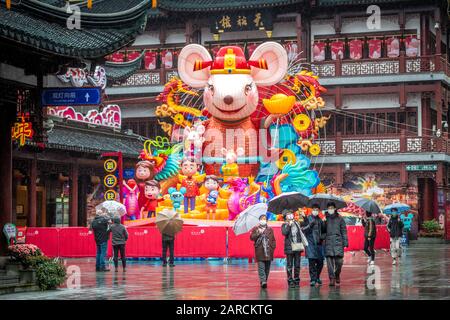 Shanghai, China, 25th Jan 2020, People wearing masks walk with umbrellas with Chinese New Year celebration reminders around them Stock Photo