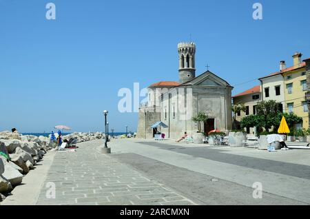 Piran, Slovenia - July 4th 2015: Unidentified people relaxing in front of medieval church Sveti Klementa in the picturesque village on Adriatic sea Stock Photo