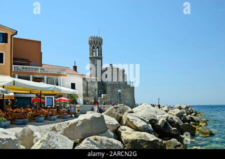 Piran, Slovenia - July 4th 2015: Unidentified people and medieval church Sveti Klementa in the picturesque village on Adriatic sea Stock Photo