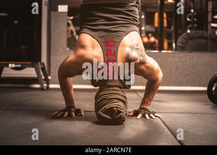 A Man in the gym is doing Yoga exercises. Kapalasana position on the head. Sleeveless t-shirt with red print: 2020 Stock Photo