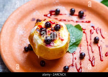 Baked Apple with blueberries. A clay saucer. Nearby is the mint leaves.  The plate stands on a textured gray canvas. Stock Photo