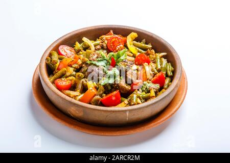 Chicken liver with vegetables on a clay plate. Pieces of liver, onion, string beans, tomato. Textured Grey canvas. Around the plate is green and red c Stock Photo