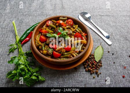 Chicken liver with vegetables on a clay plate. Pieces of liver, onion, string beans, tomato. Textured Grey canvas. Around the plate is green and red c Stock Photo