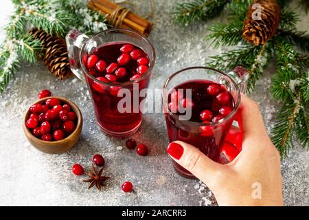 Christmas drinks. Female hand holding of Hot winter drink with cranberries and cinnamon on a light stone table. Stock Photo