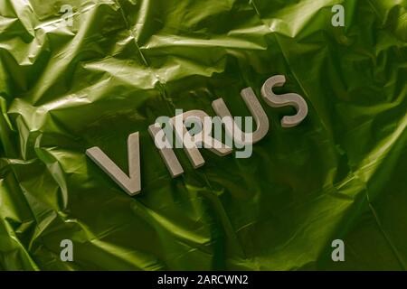 the word virus laid with silver metal letters on crumpled green plastic film with dramatic light Stock Photo