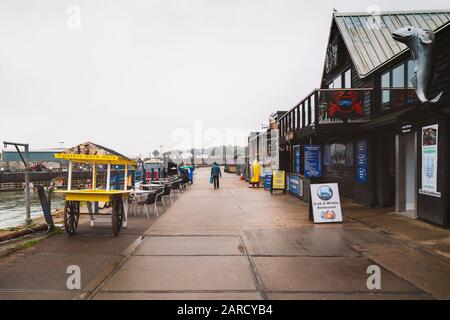 Whitstable, England - Jan 24 2020 A small fresh oyster cart, restaurants and their alfresco tables along the Whitstable harbour on a damp winter day. Stock Photo