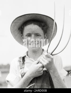 1930s  SMILING FRECKLE-FACED FARM BOY WEARING STRAW HAT WORK CLOTHES HOLDING A PITCHFORK LOOKING AT CAMERA  - b11180 HAR001 HARS PLEASED JOY LIFESTYLE SATISFACTION JOBS HEALTHINESS HOME LIFE COPY SPACE HALF-LENGTH PERSONS INSPIRATION OVERALLS FARMING MALES FRECKLES CONFIDENCE EXPRESSIONS AGRICULTURE B&W EYE CONTACT SKILL OCCUPATION HAPPINESS SKILLS CHEERFUL PITCHFORK FARMERS PRIDE OCCUPATIONS SMILES JOYFUL TEENAGED COOPERATION GROWTH JUVENILES PRE-TEEN PRE-TEEN BOY BLACK AND WHITE CAUCASIAN ETHNICITY FRECKLE-FACED HAR001 OLD FASHIONED Stock Photo